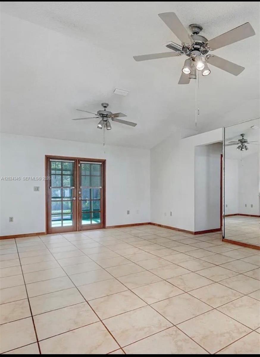 An empty room features white walls, light-colored tile flooring, two ceiling fans, and glass doors — 112 SE Vin Rose Cir, Palm Bay FL 32909, PALM BAY, FL