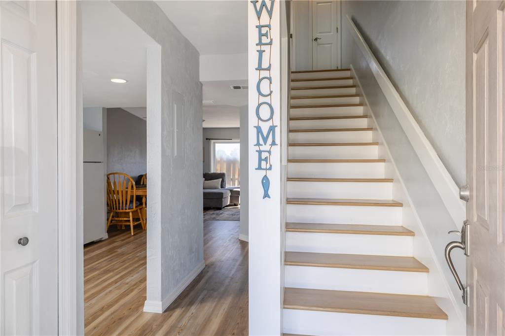 An entryway features a staircase with light wood treads, white risers, and a vertical welcome sign — 4786 S ATLANTIC AVENUE UNIT 4B, PONCE INLET, FL