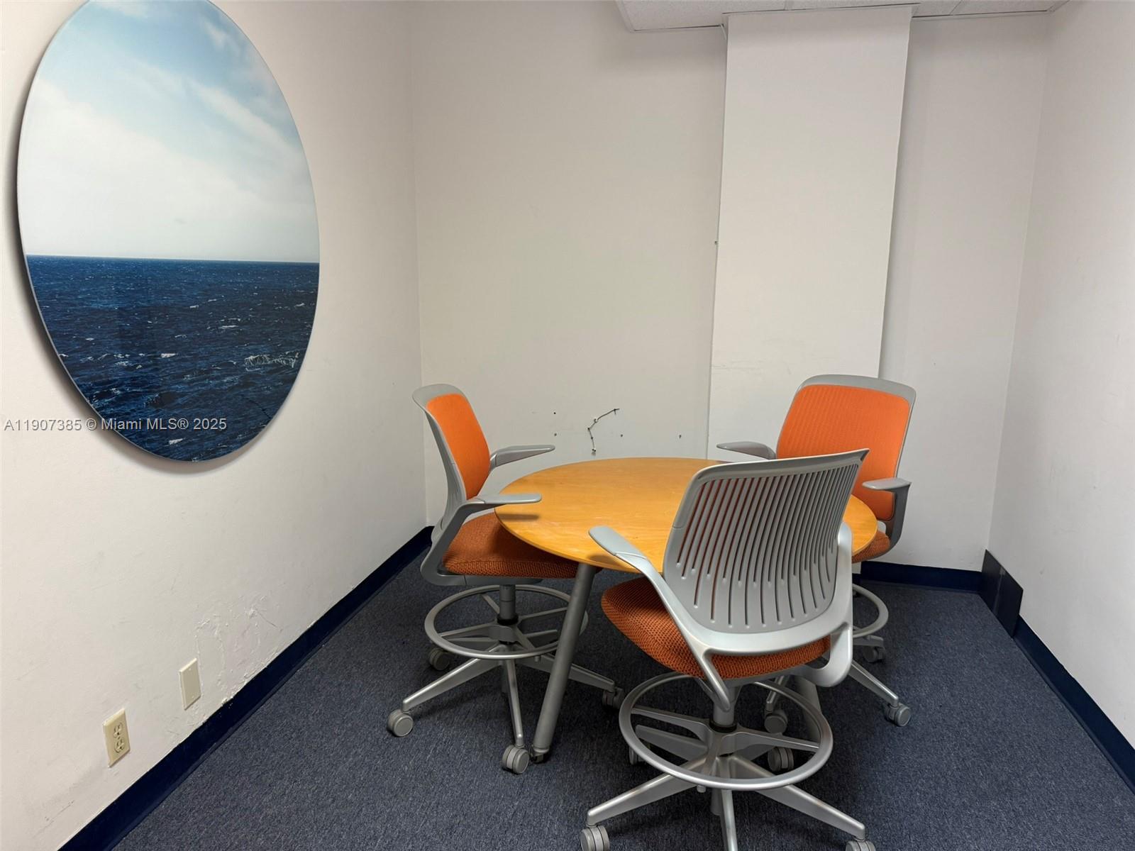 A small meeting room features a round wooden table, three orange chairs, and circular wall art — 220 Miracle Mile # B236, Coral Gables FL 33134, CORAL GABLES, FL