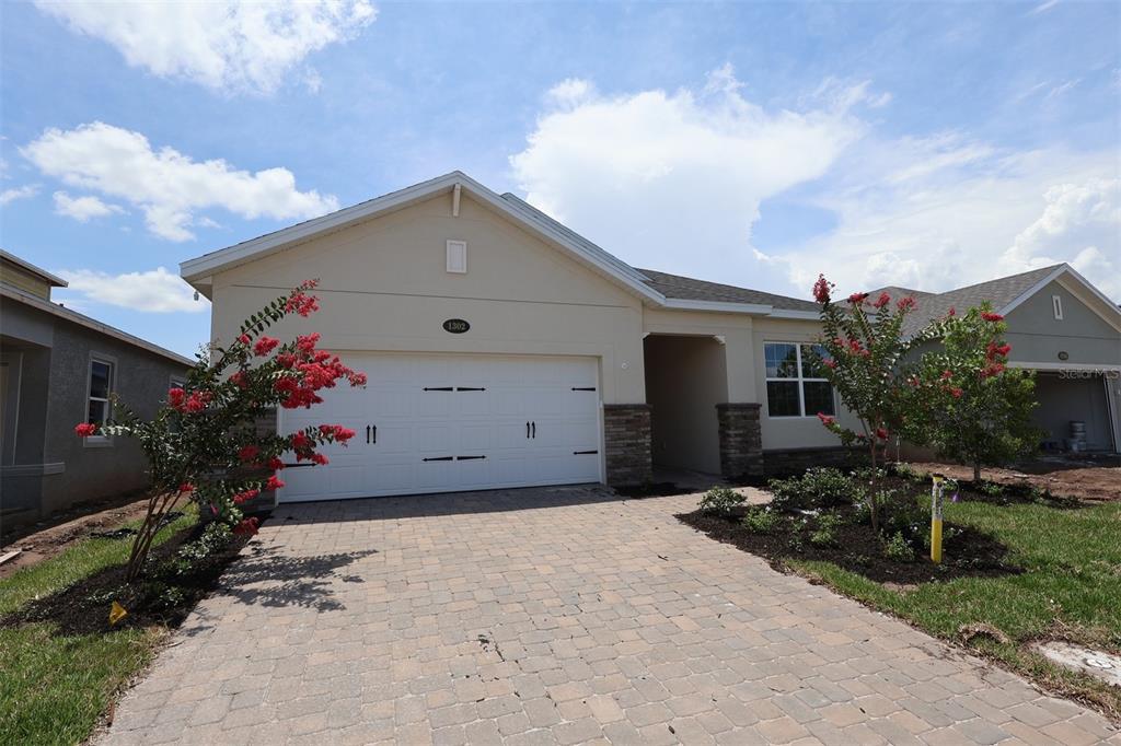 A single-story house with a beige stucco exterior, a paved driveway, and blooming crape myrtles — 1302 HYDE STREET, ST CLOUD, FL