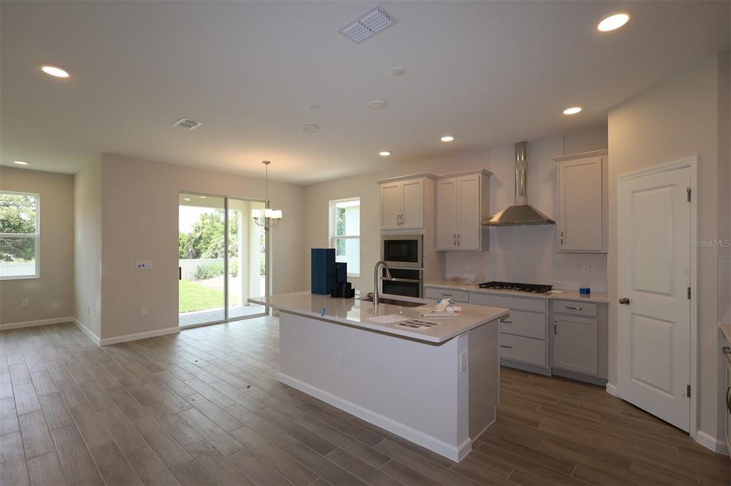 A modern kitchen features a central island, grey cabinetry, stainless steel appliances, and tile flooring — 1302 HYDE STREET, ST CLOUD, FL
