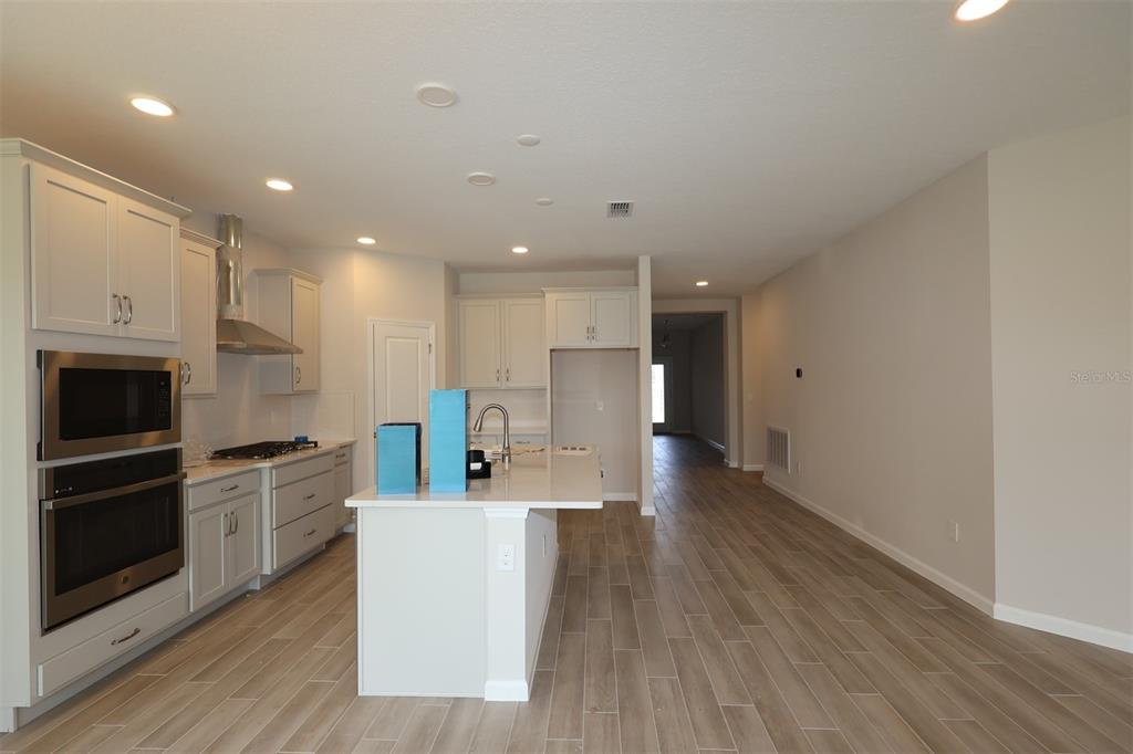 A modern kitchen features white cabinetry, stainless steel appliances, a center island, and wood-look flooring — 1302 HYDE STREET, ST CLOUD, FL