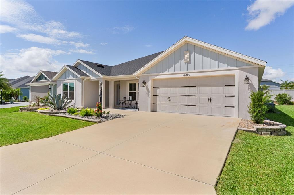 A single-story house with a beige stucco exterior, a two-car garage, and a landscaped yard — 6692 NEWELL LOOP, THE VILLAGES, FL