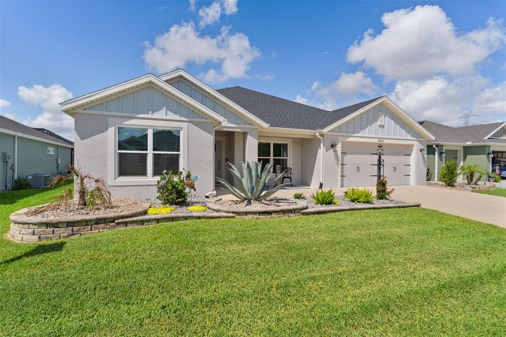 A single-story suburban house with a beige stucco exterior, gabled roof, and landscaped front yard — 6692 NEWELL LOOP, THE VILLAGES, FL