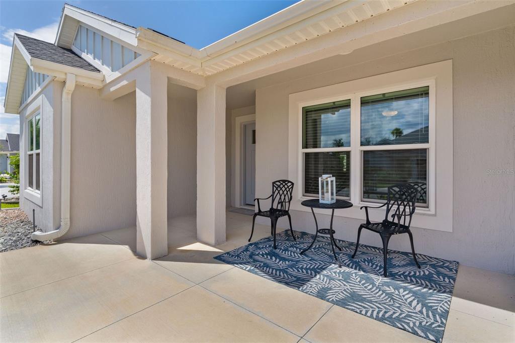 A covered concrete porch features two black metal chairs, a small table, and a rug — 6692 NEWELL LOOP, THE VILLAGES, FL