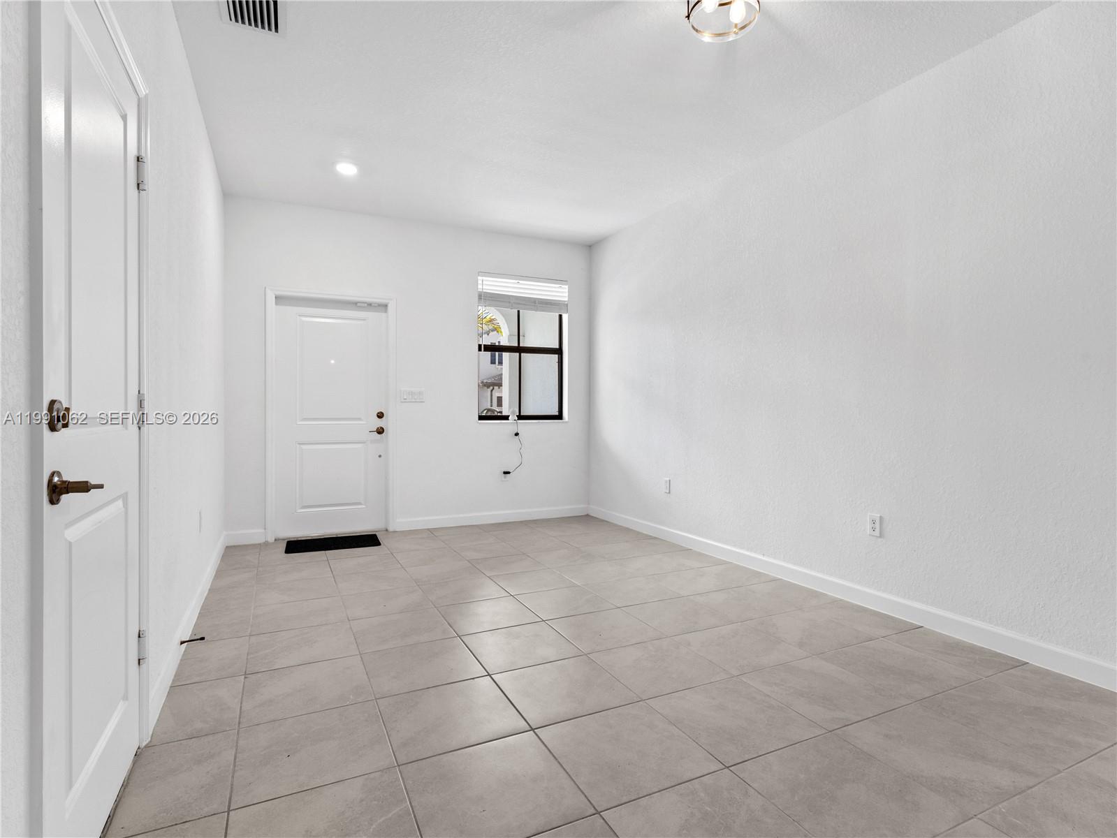 An empty room features white walls, light-colored tile flooring, a window, and two doors — 28562 SW 134th Ct, Miami FL 33033, MIAMI, FL
