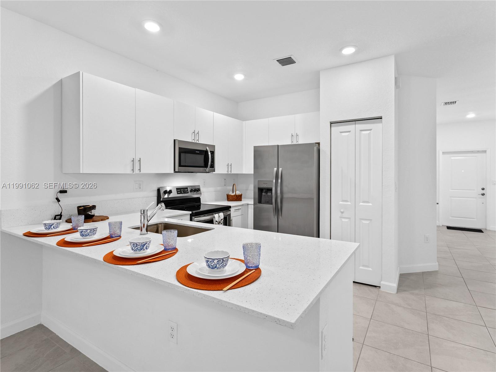A modern kitchen features white cabinets, stainless steel appliances, and a white quartz breakfast bar — 28562 SW 134th Ct, Miami FL 33033, MIAMI, FL