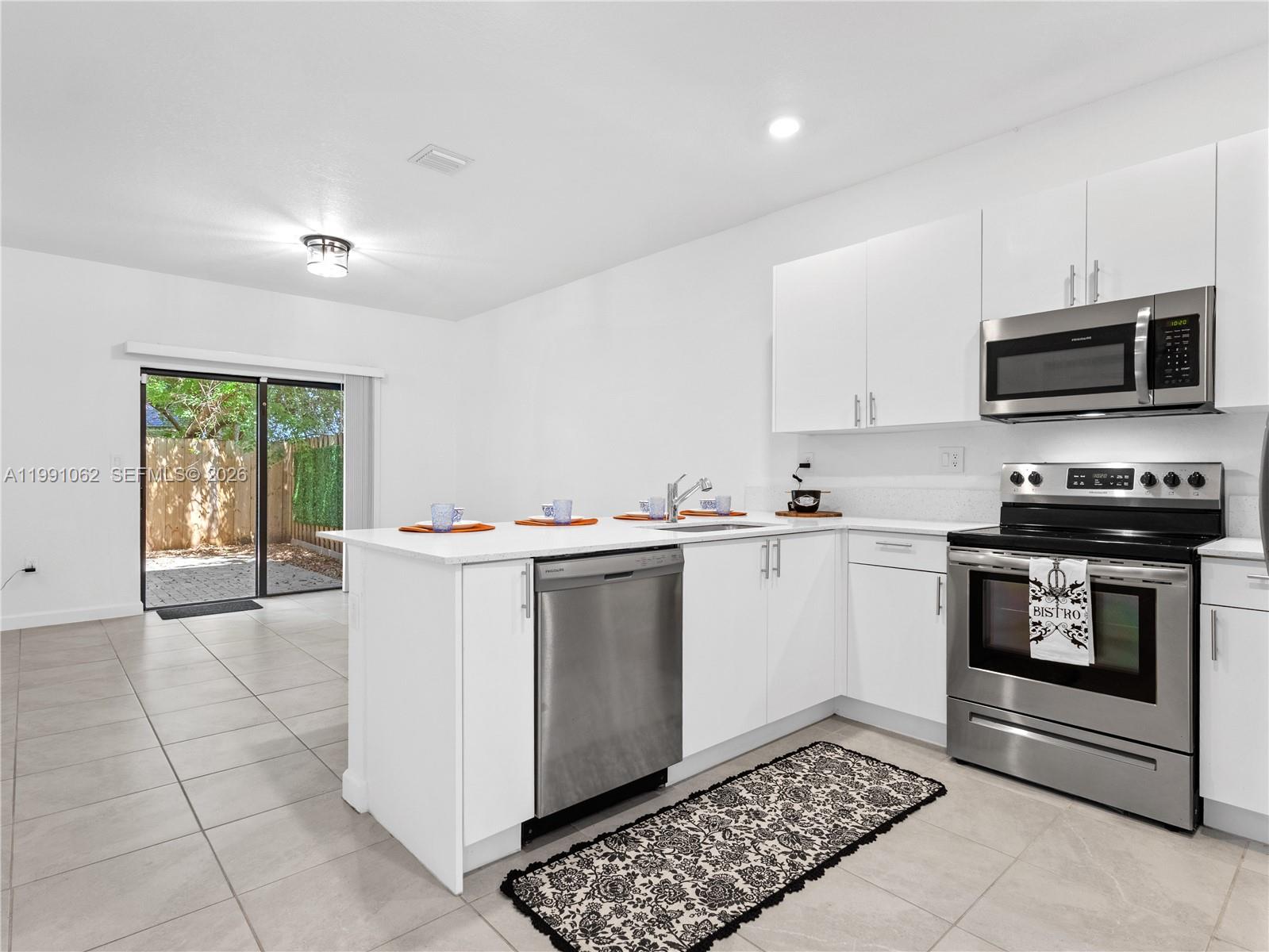 A modern kitchen features white cabinets, stainless steel appliances, and a sliding glass door — 28562 SW 134th Ct, Miami FL 33033, MIAMI, FL