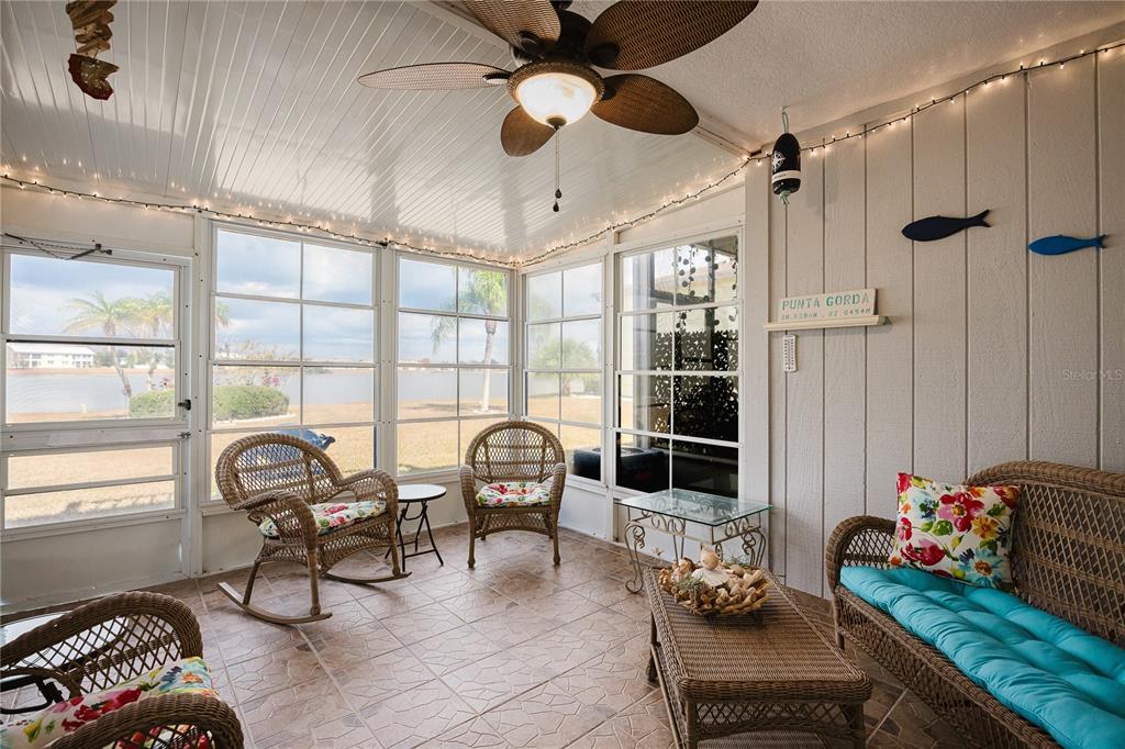 A sunroom features wicker furniture, tile flooring, a ceiling fan, and views of a lake — 26282 RAMPART BOULEVARD UNIT 204, PUNTA GORDA, FL