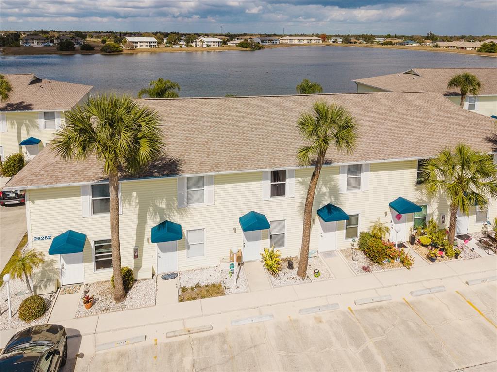 An aerial view shows a yellow multi-unit residential building with palm trees and a lake — 26282 RAMPART BOULEVARD UNIT 204, PUNTA GORDA, FL