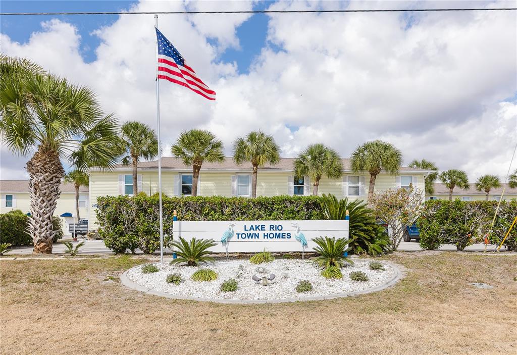 A sign for Lake Rio Town Homes stands in front of a yellow residential building — 26282 RAMPART BOULEVARD UNIT 204, PUNTA GORDA, FL