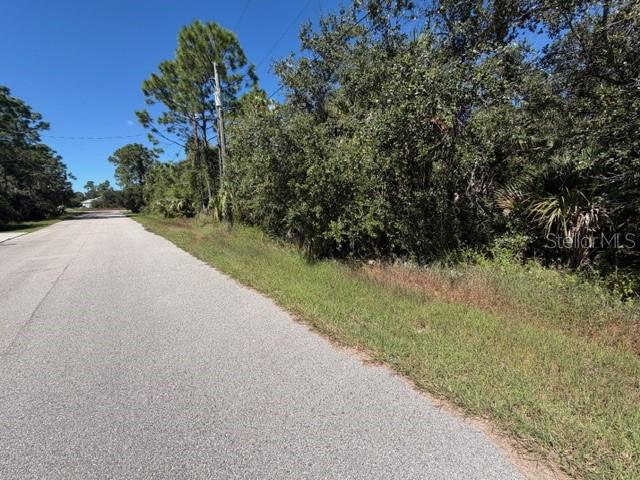 A paved road runs alongside a vacant, wooded lot under a clear blue sky — Lot 3 BERNHARD ROAD, NORTH PORT, FL