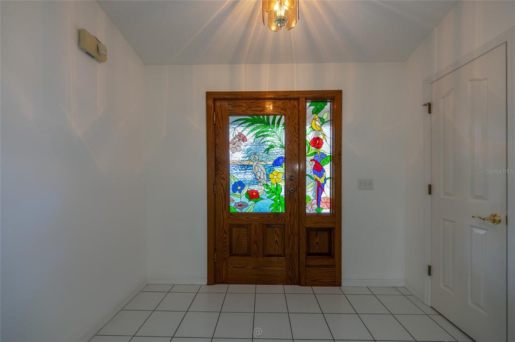An entryway features white tiled floors, plain white walls, and a decorative stained-glass wooden door — 29 WOOD HAVEN DRIVE, PALM COAST, FL