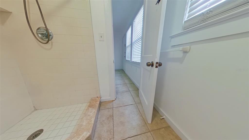 A tiled shower stall sits next to an open doorway leading to a sunlit hallway — 327 NW 15TH TERRACE, GAINESVILLE, FL
