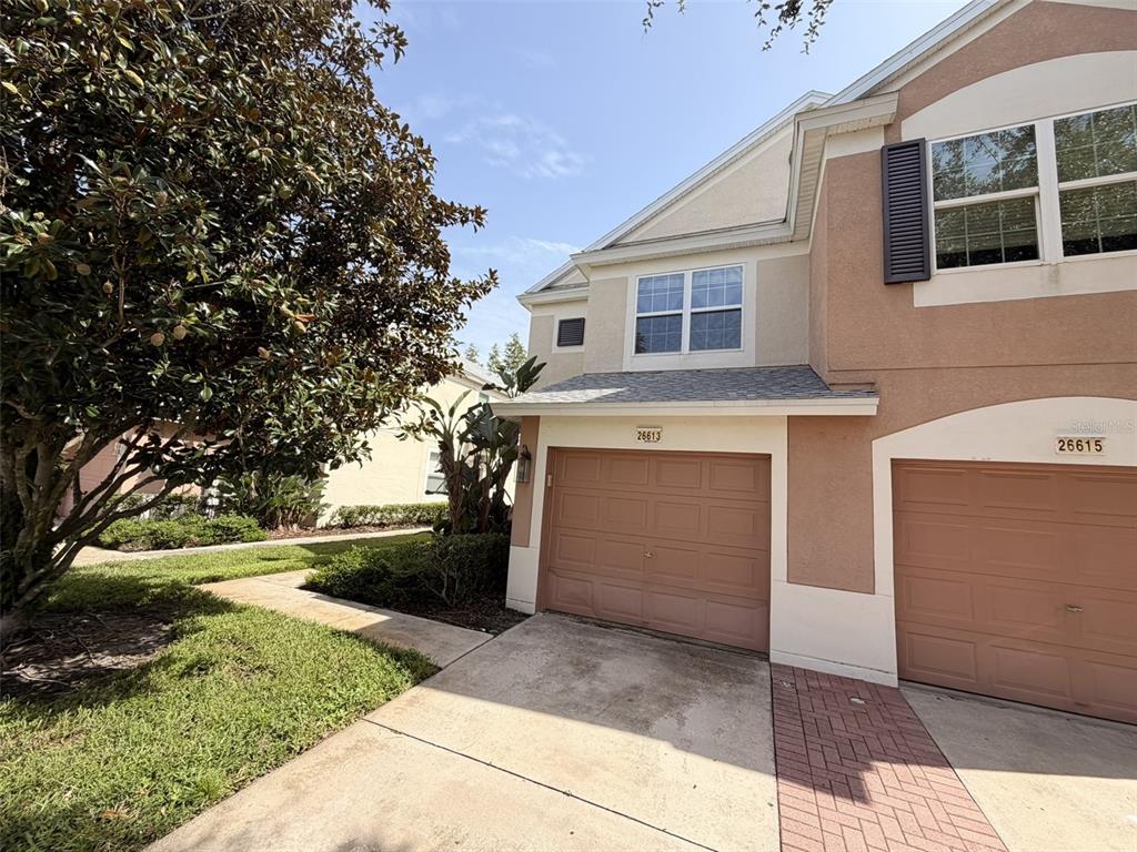 A two-story townhouse exterior features tan stucco walls, two garage doors, and a paved driveway — 26613 CASTLEVIEW WAY, WESLEY CHAPEL, FL