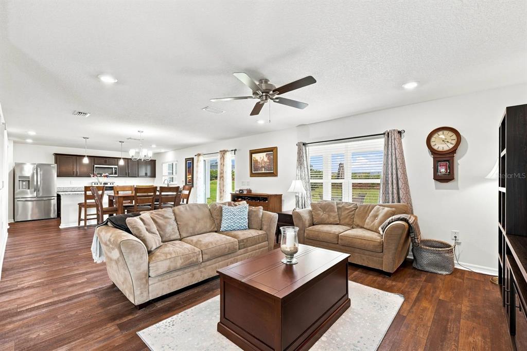 A living room with wood-look flooring, a brown sofa and loveseat, and an open kitchen — 455 OVERPOOL AVENUE, DAVENPORT, FL