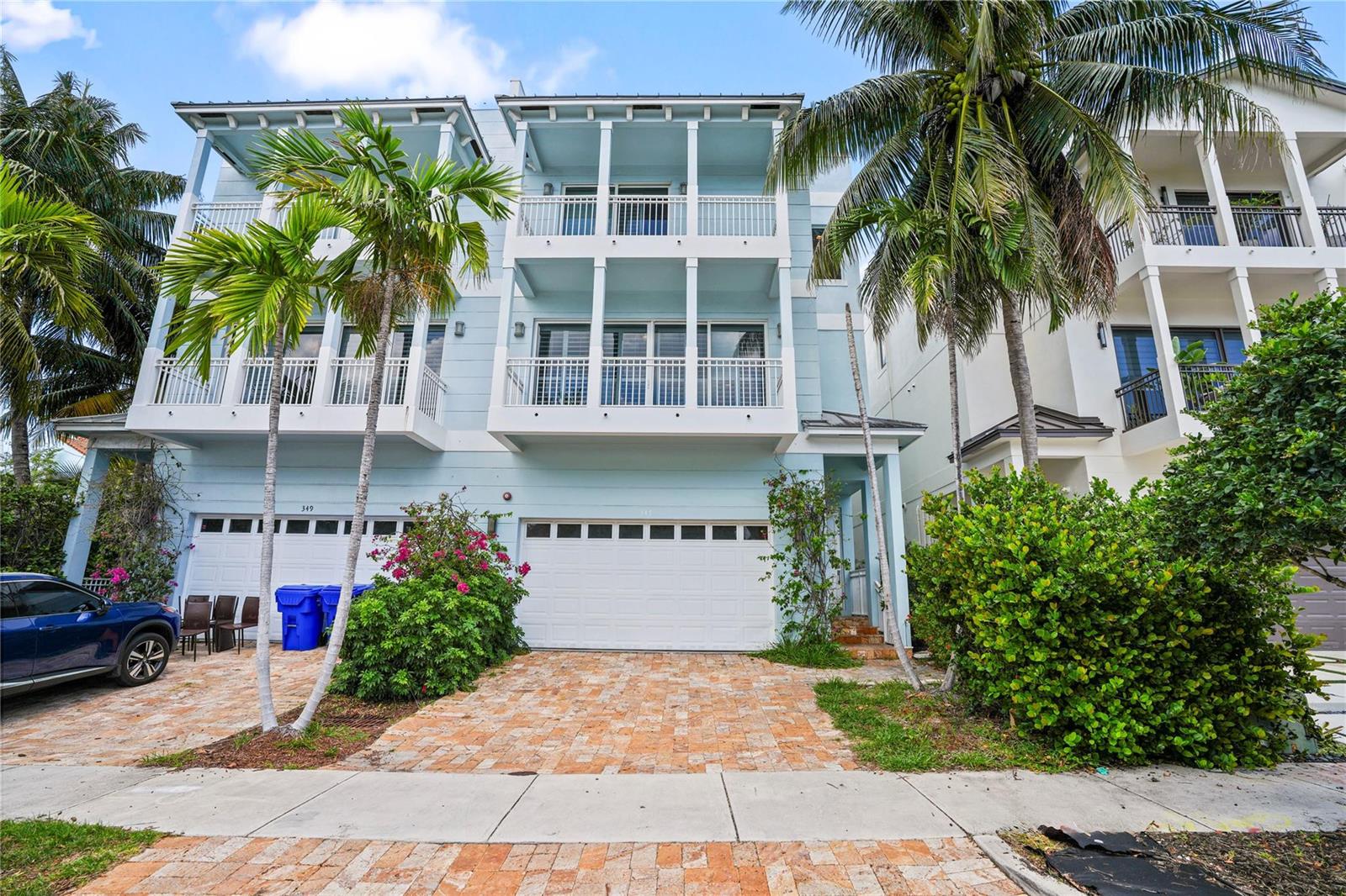 A three-story light blue townhouse features a two-car garage and balconies with white railings — 347 Oak Street # B1, Hollywood FL 33019, HOLLYWOOD, FL