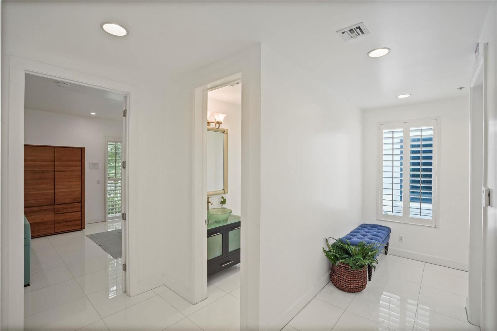 A bright hallway with white tile floors, a blue bench, and a view into a bathroom — 347 Oak Street # B1, Hollywood FL 33019, HOLLYWOOD, FL
