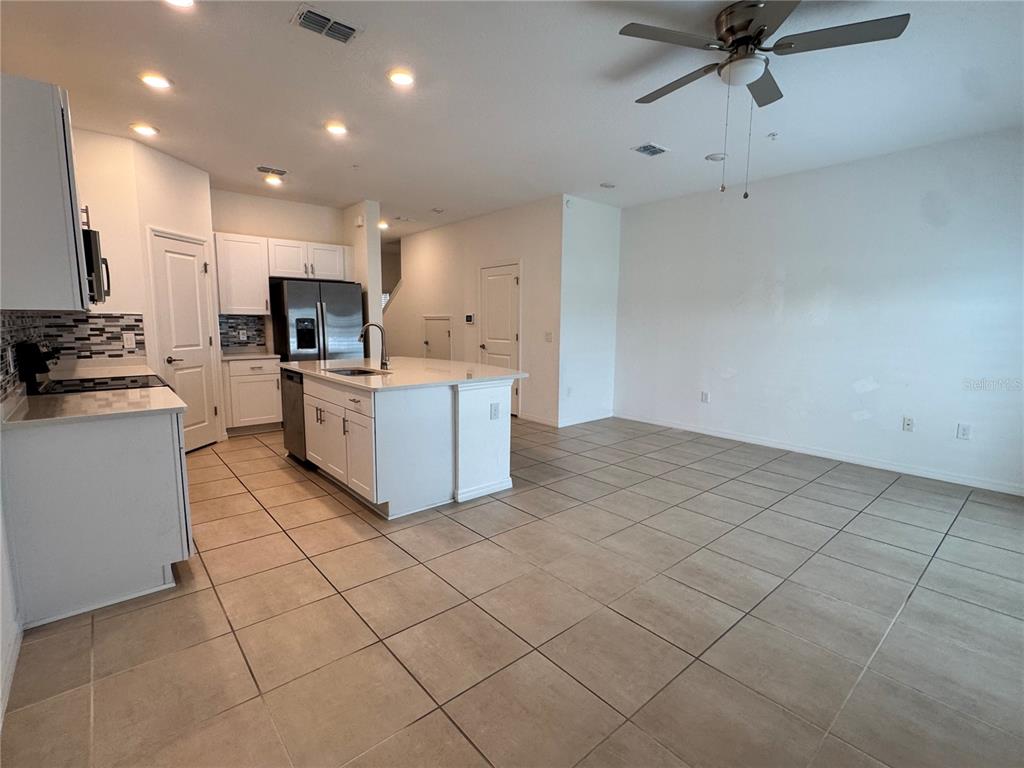 A kitchen with white cabinets and a center island opens into a large tiled room — 4461 ARLINGTON AVENUE, ST CLOUD, FL