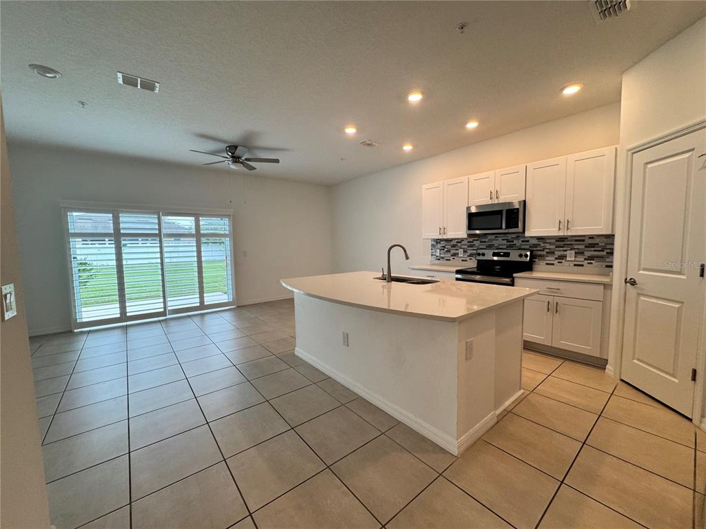 A kitchen with white cabinets, a central island, and tile flooring opens to a living area — 4461 ARLINGTON AVENUE, ST CLOUD, FL