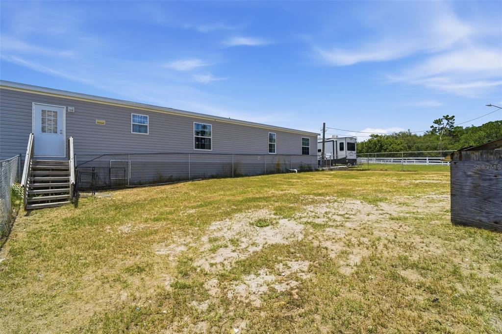 The exterior of a light gray manufactured home features a wooden staircase and fenced yard — 7242 BLACK ROAD, LAKE WALES, FL