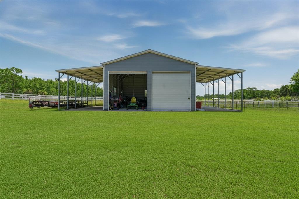 A detached metal garage with two open-sided carports sits on a large grassy lawn — 7242 BLACK ROAD, LAKE WALES, FL