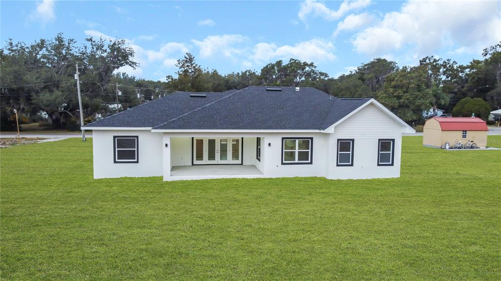 The rear exterior of a white single-story house with a covered patio and dark trim — 5530 BELL, ZEPHYRHILLS, FL