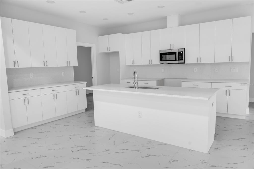A modern kitchen featuring white cabinets, a central island with a sink, and marble-patterned flooring — 5530 BELL, ZEPHYRHILLS, FL