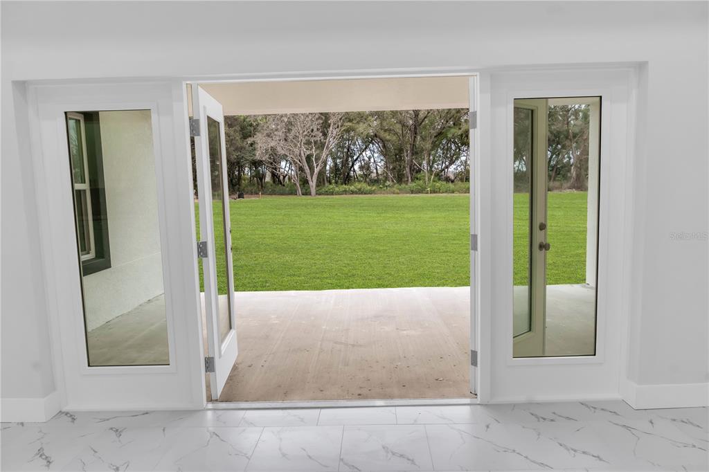 A view from inside looking through open glass doors onto a concrete patio and lawn — 5530 BELL, ZEPHYRHILLS, FL