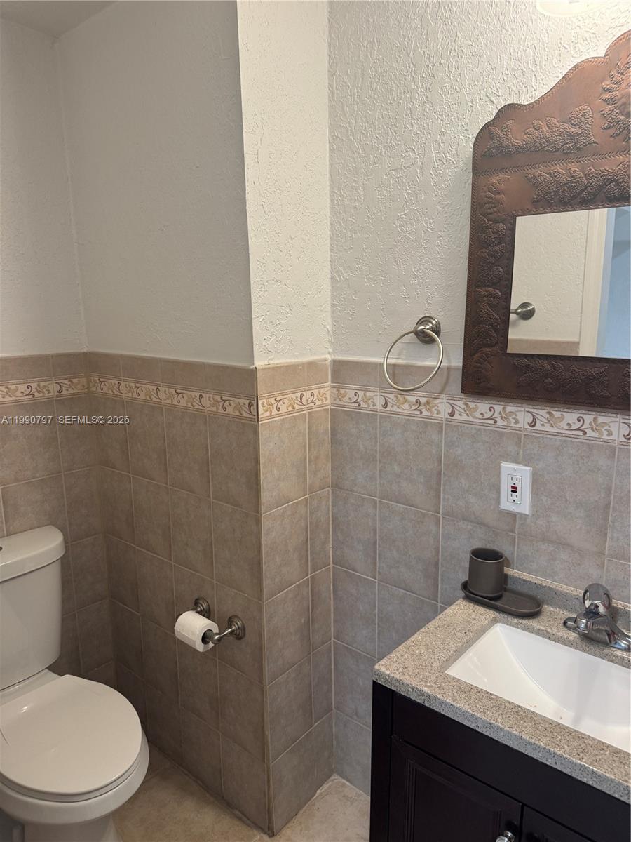 A bathroom features a vanity with a granite countertop, a toilet, and tiled walls — 6126 SW 61st St, South Miami FL 33143, SOUTH MIAMI, FL