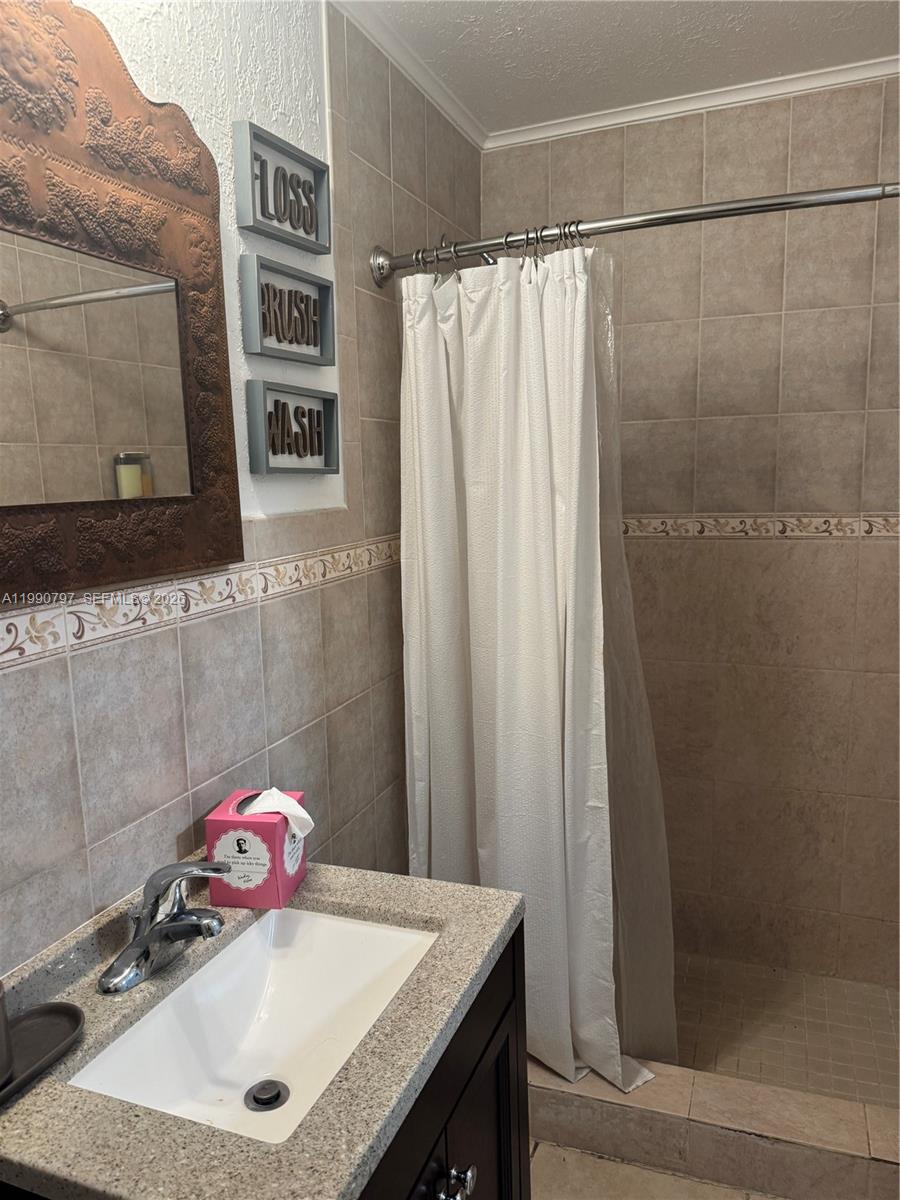 A bathroom features a vanity with a granite countertop, tiled walls, and a shower curtain — 6126 SW 61st St, South Miami FL 33143, SOUTH MIAMI, FL