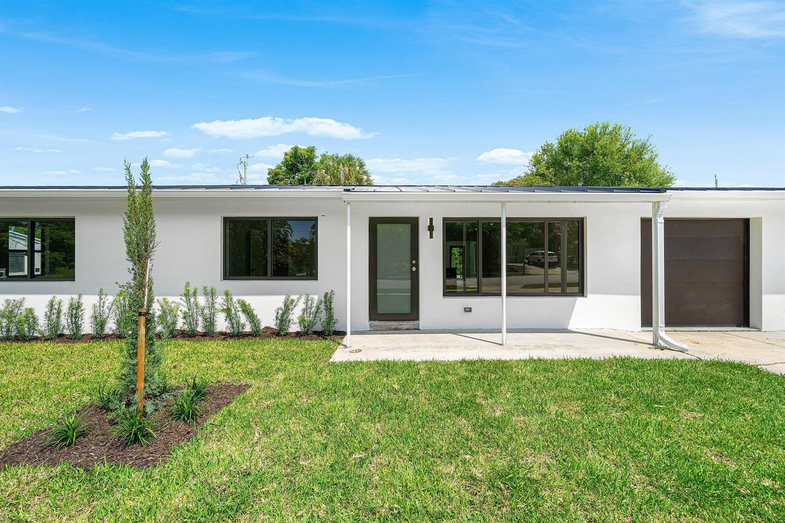A single-story white house with a flat roof, dark-framed windows, and a front lawn — 707 Sunset Drive, FL 33461, FL