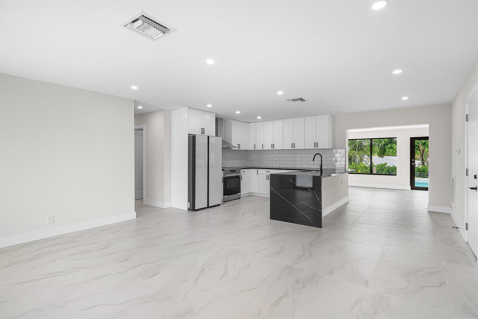 A modern kitchen features white cabinets, a black marble island, and light-colored tile flooring — 707 Sunset Drive, FL 33461, FL