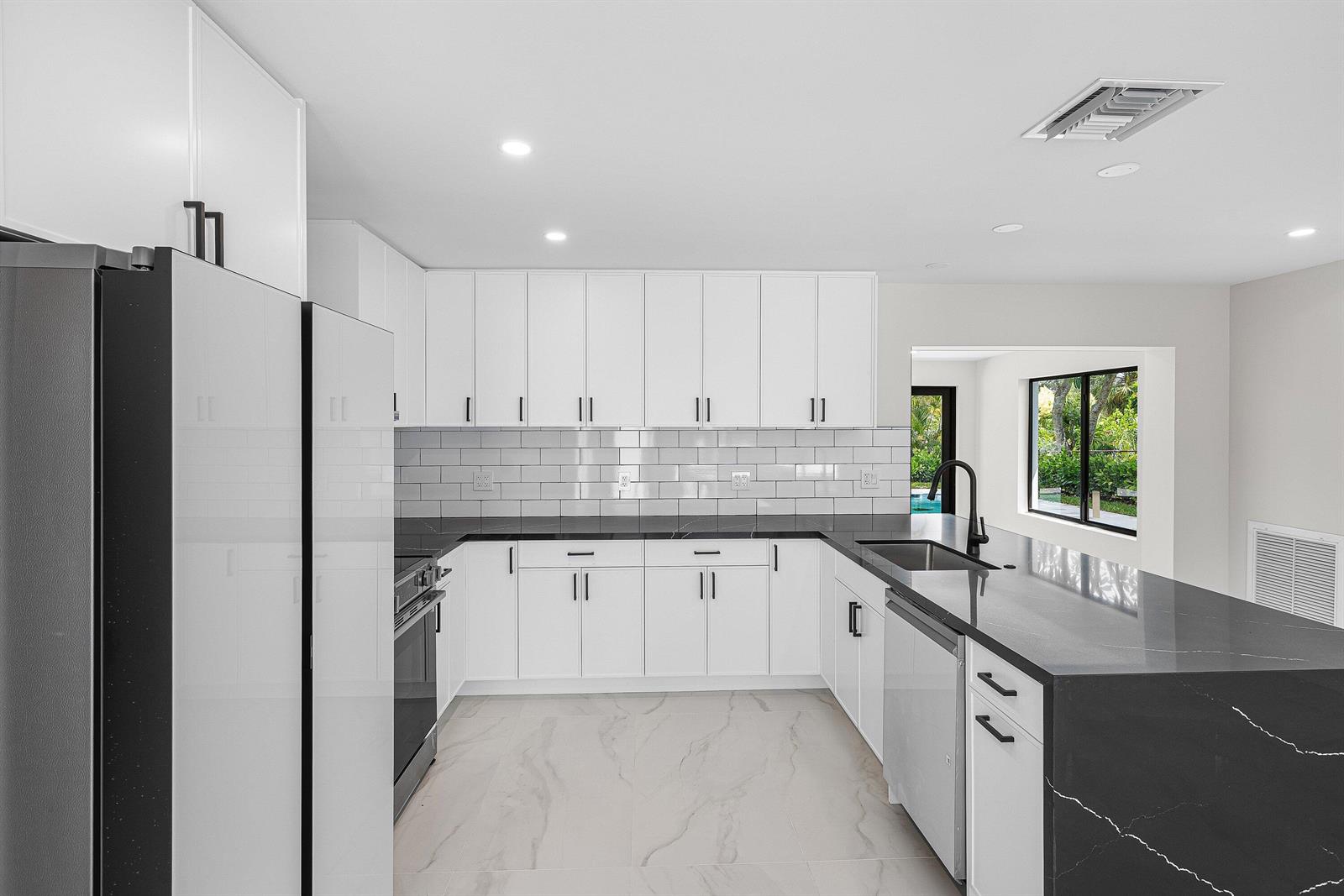 A modern kitchen features white cabinets, black countertops, a subway tile backsplash, and marble flooring — 707 Sunset Drive, FL 33461, FL