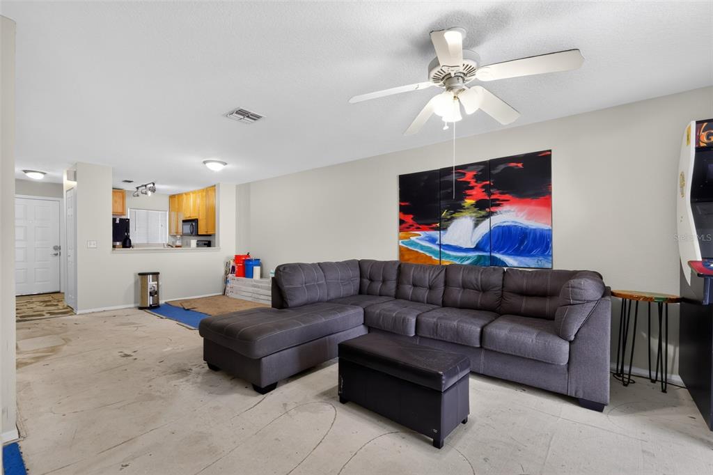 A living room features a gray sectional sofa, a ceiling fan, and unfinished concrete flooring — 3 ARBOR CLUB DRIVE UNIT 212, PONTE VEDRA BEACH, FL