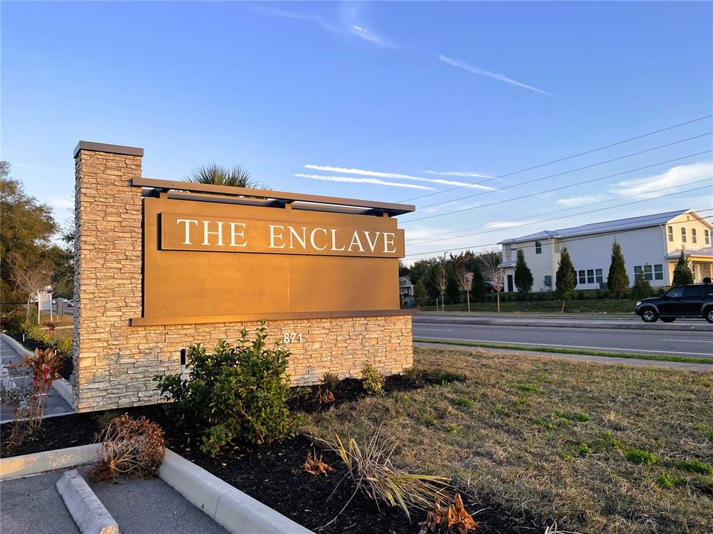 A stone monument sign for The Enclave stands beside a road with a house nearby — 871 HIGHWAY 466, LADY LAKE, FL