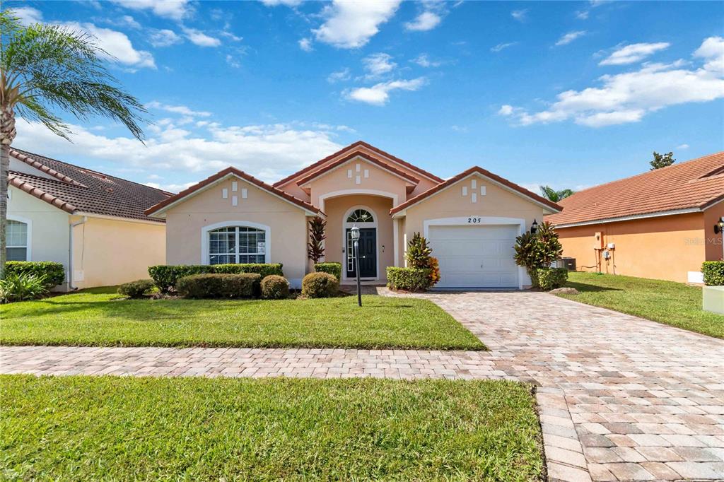 A single-story house with a tan stucco exterior, a tiled roof, and a paved driveway — 205 HUMMINGBIRD PASS, DAVENPORT, FL