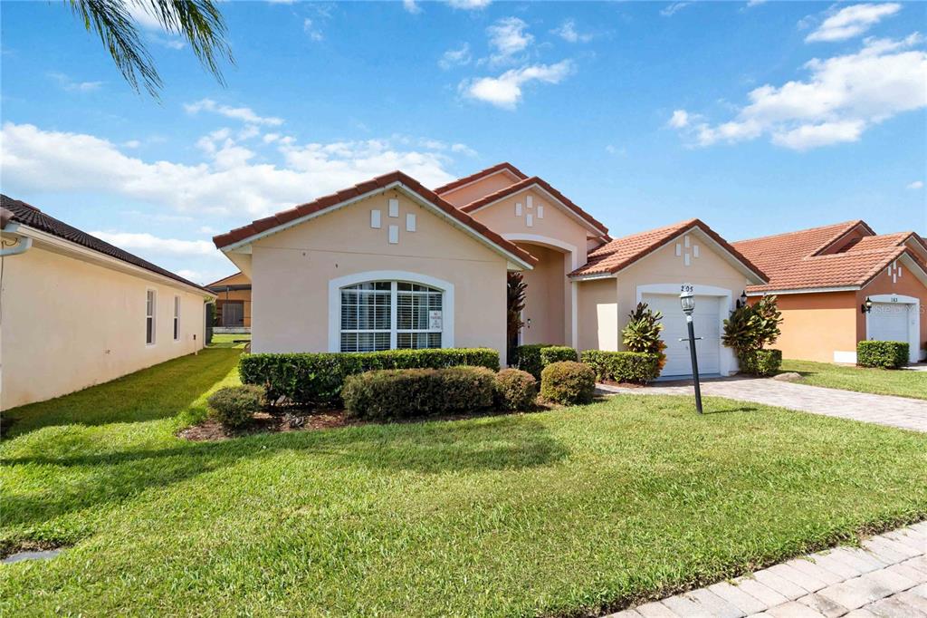 A single-story house with a beige stucco exterior, a tiled roof, and a front lawn — 205 HUMMINGBIRD PASS, DAVENPORT, FL