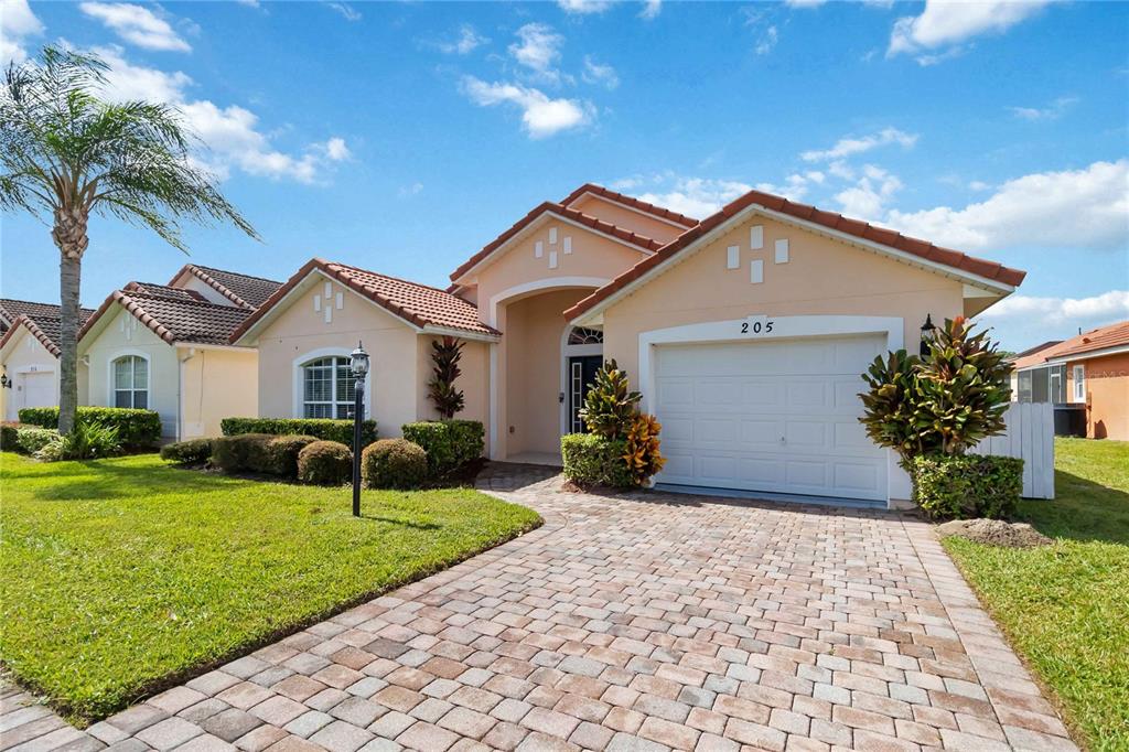 A single-story suburban house features a paver driveway, a two-car garage, and a tiled roof — 205 HUMMINGBIRD PASS, DAVENPORT, FL