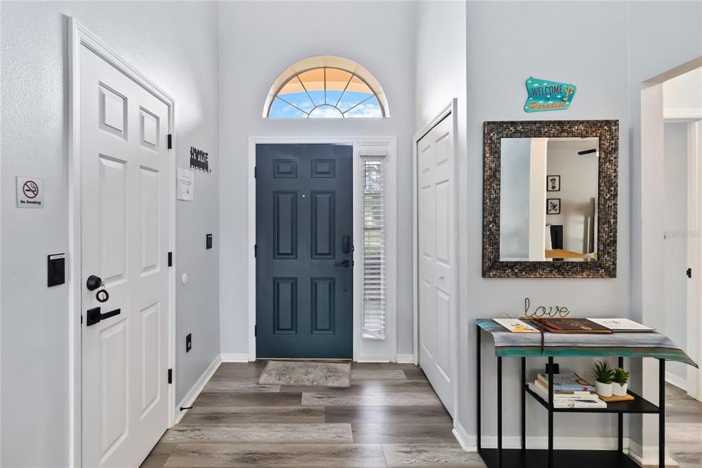A bright entryway features a dark blue front door, light wood flooring, and a wall mirror — 205 HUMMINGBIRD PASS, DAVENPORT, FL