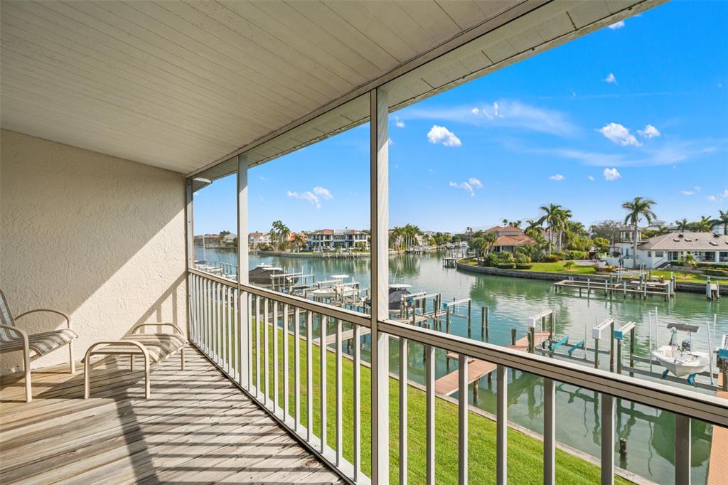 A screened-in balcony with wooden flooring overlooks a canal lined with boat docks and houses — 637 PINELLAS BAYWAY S UNIT 111, ST PETERSBURG, FL