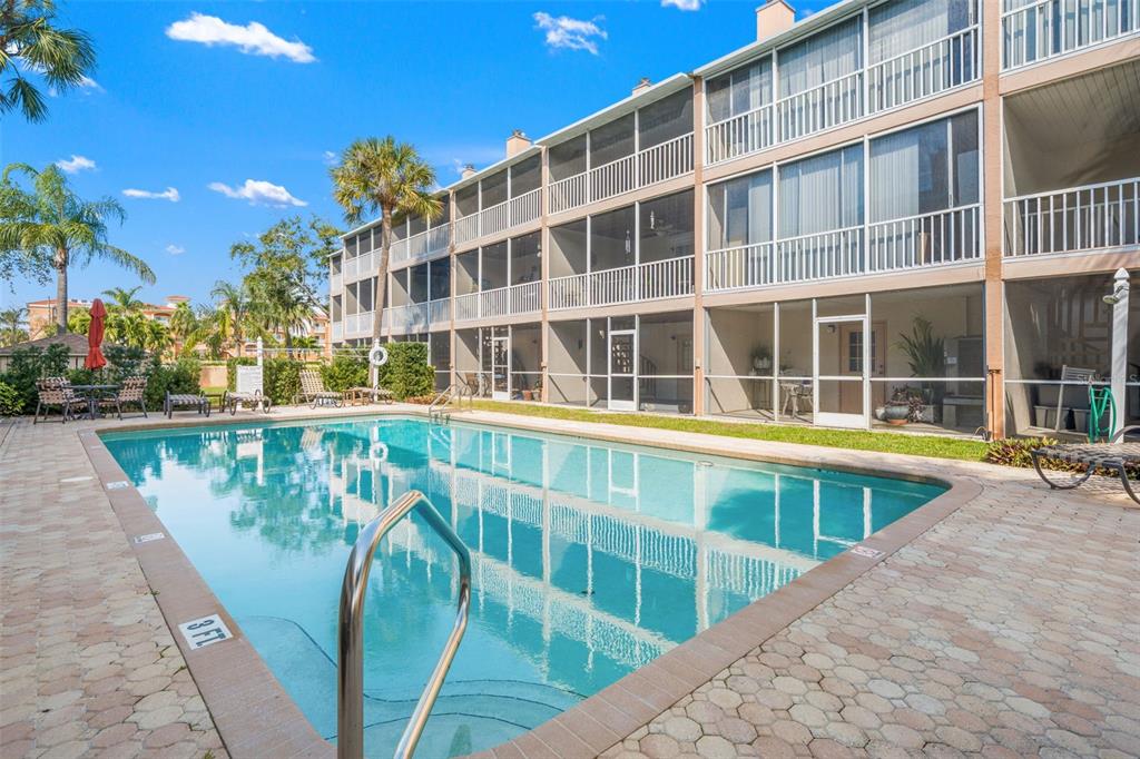 A rectangular swimming pool sits in front of a three-story apartment building with screened balconies — 637 PINELLAS BAYWAY S UNIT 111, ST PETERSBURG, FL