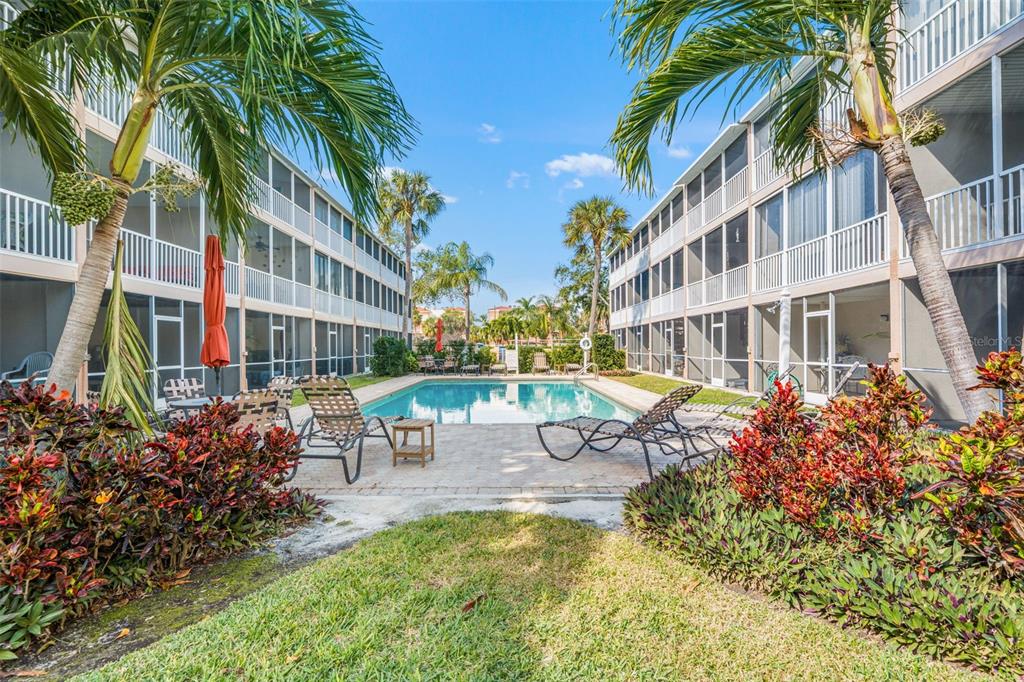 A swimming pool sits between two multi-story apartment buildings with screened balconies and palm trees — 637 PINELLAS BAYWAY S UNIT 111, ST PETERSBURG, FL