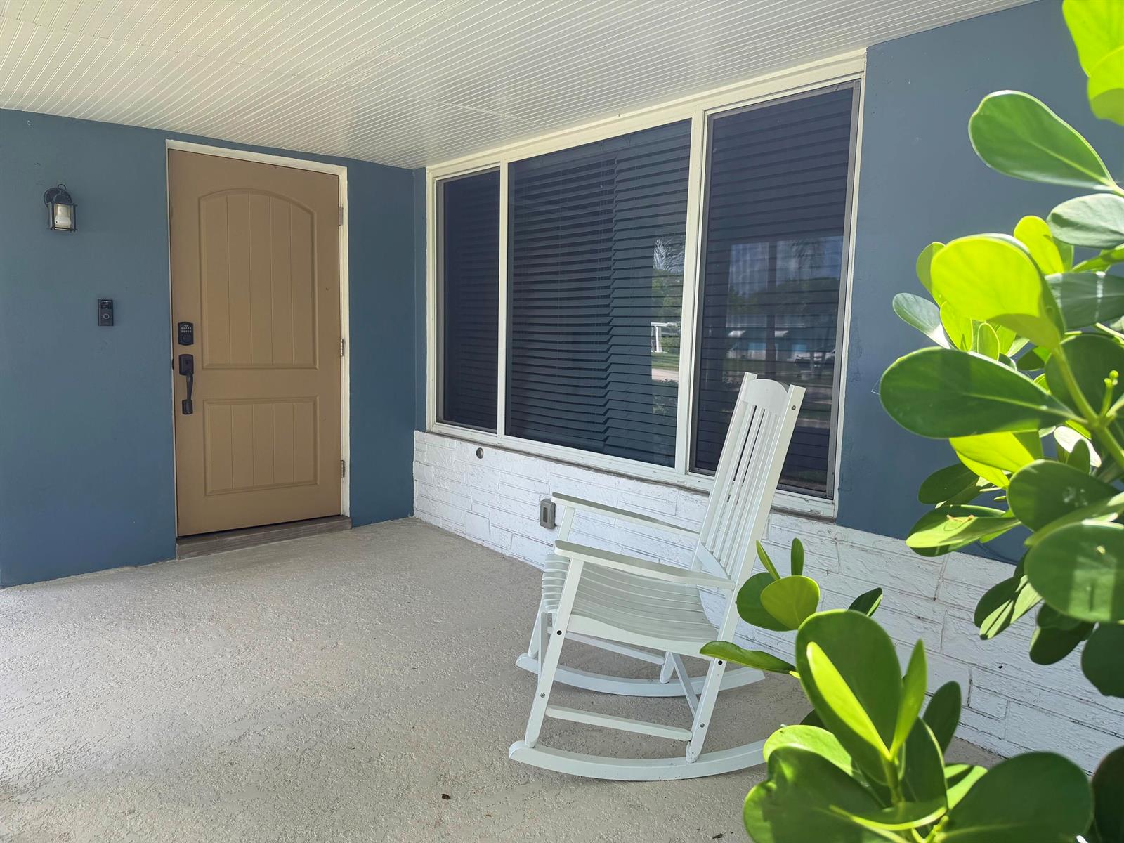 A covered porch features a tan front door, a white rocking chair, and blue siding — 1516 NW 58th Avenue, Margate FL 33063, MARGATE, FL