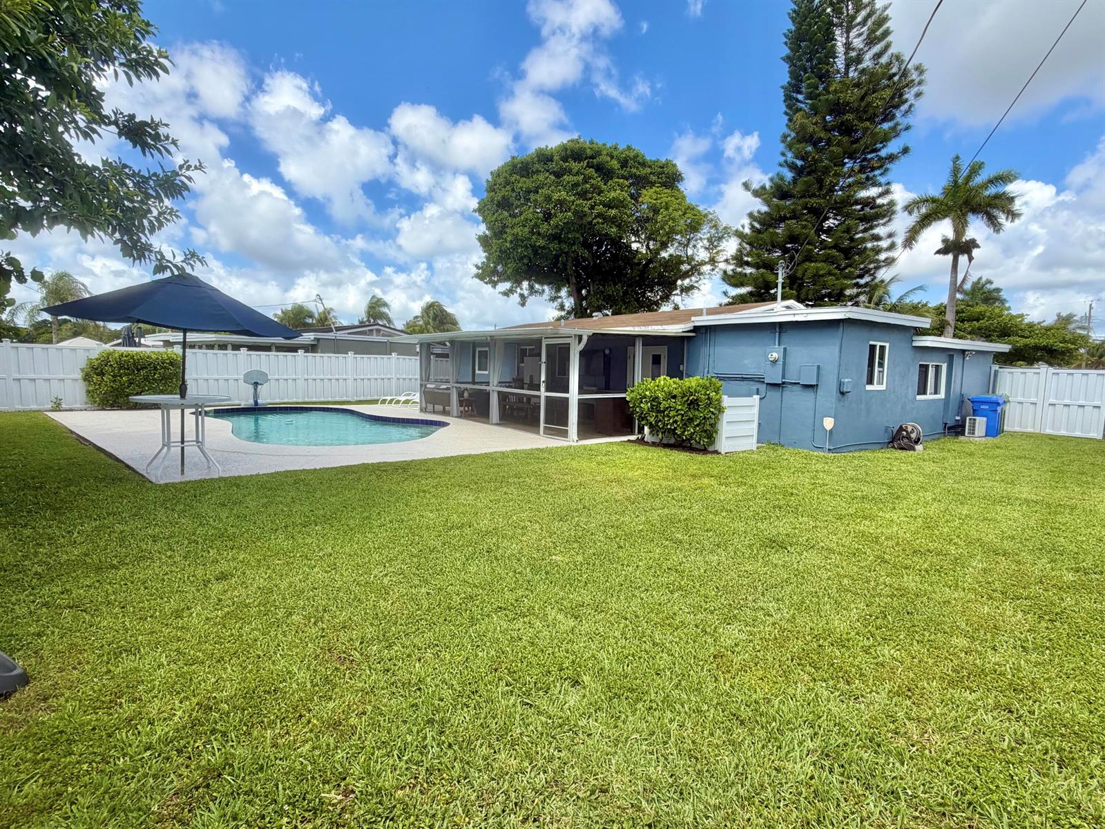 A blue house with a screened-in patio, swimming pool, and large backyard under a blue sky — 1516 NW 58th Avenue, Margate FL 33063, MARGATE, FL
