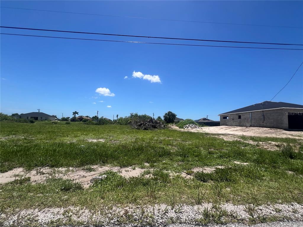 A vacant, grassy residential lot sits under a clear blue sky next to a house — 2208 NE 6TH AVENUE, CAPE CORAL, FL