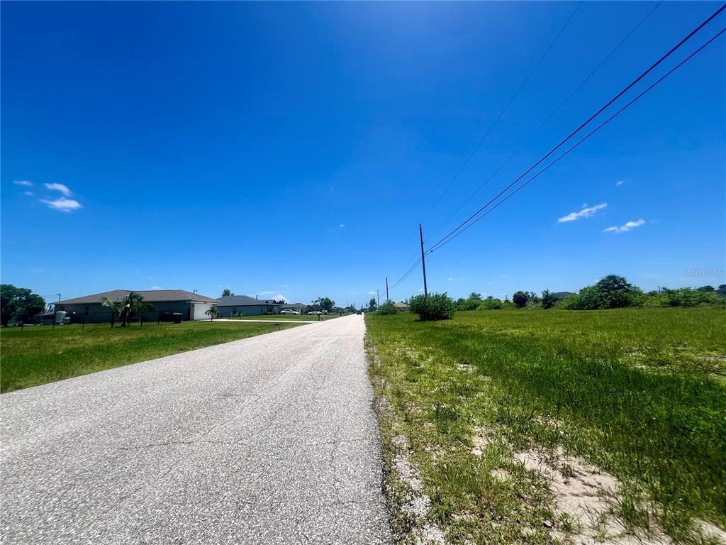 A paved road stretches between a residential area and an open, grassy field — 2208 NE 6TH AVENUE, CAPE CORAL, FL