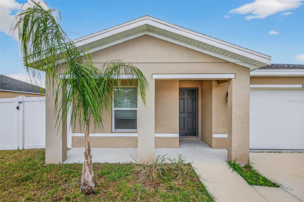 A tan single-story house exterior features a front porch, a palm tree, and a garage — 842 GILA WAY, KISSIMMEE, FL