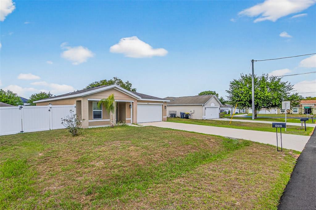 A single-story house with a white garage door, tan stucco exterior, and a white fence — 842 GILA WAY, KISSIMMEE, FL