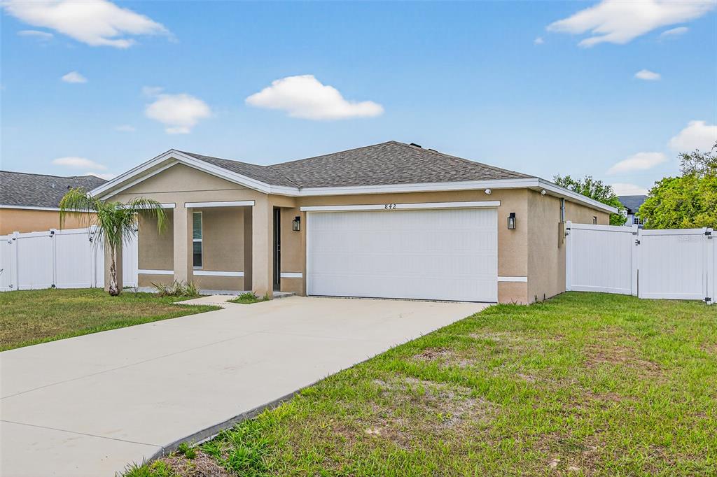 A single-story house with a beige stucco exterior, a two-car garage, and a white fence — 842 GILA WAY, KISSIMMEE, FL